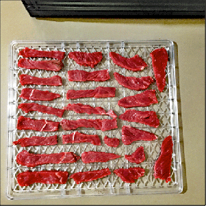 Thin slices of raw, lean meat on a dehydrator tray.